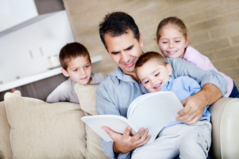 Father at home reading a book to his children